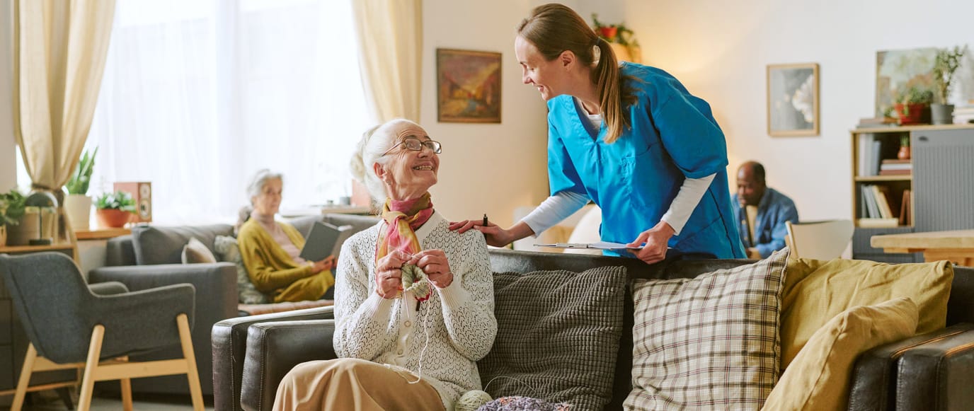 A caregiver interacts with a smiling resident in a cozy common area.