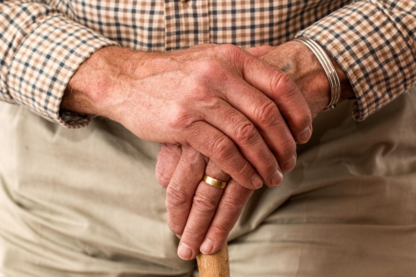 Close-up of elderly hands resting on a cane