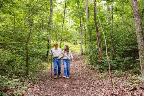 A resident and staff member strolling on a forested path