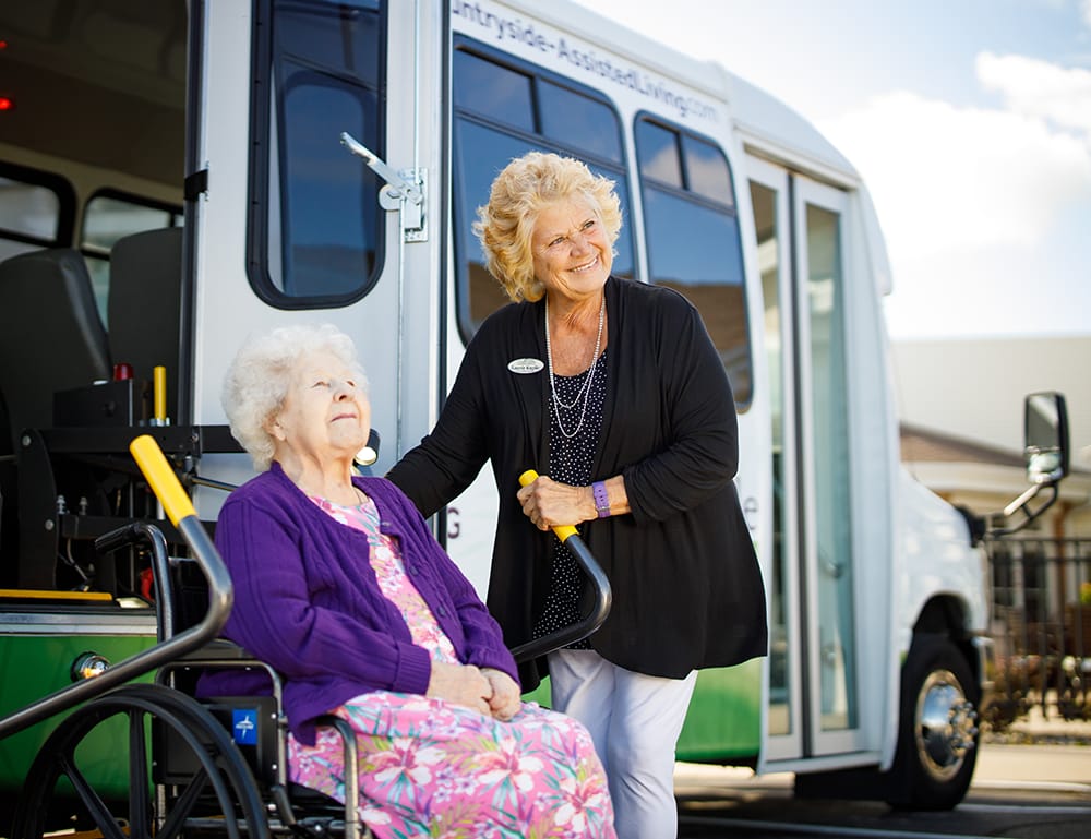 Staff assisting a resident in front of a facility transport van