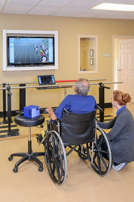 Resident in a wheelchair using a rehabilitation program with staff assistance