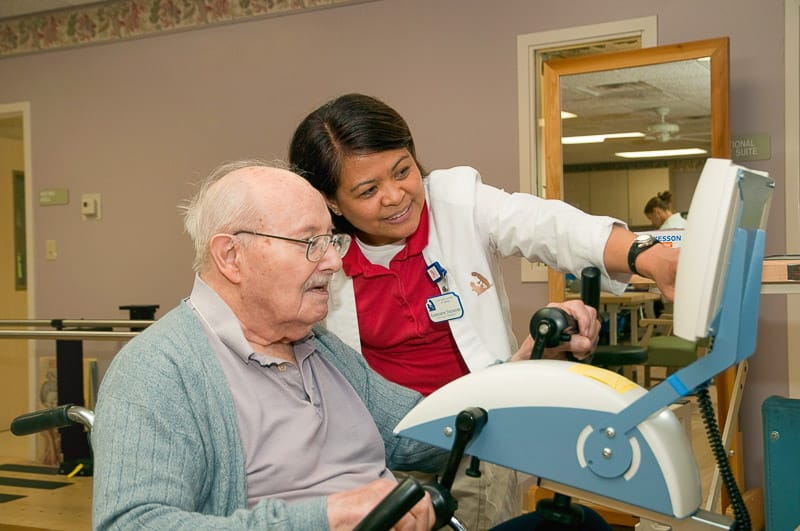 Senior resident engaging with staff on exercise equipment