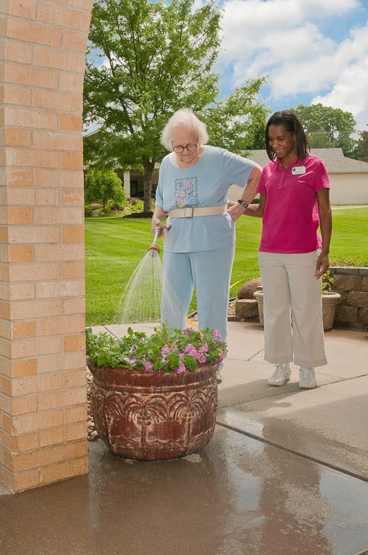 An elderly resident watering flowers with staff assistance