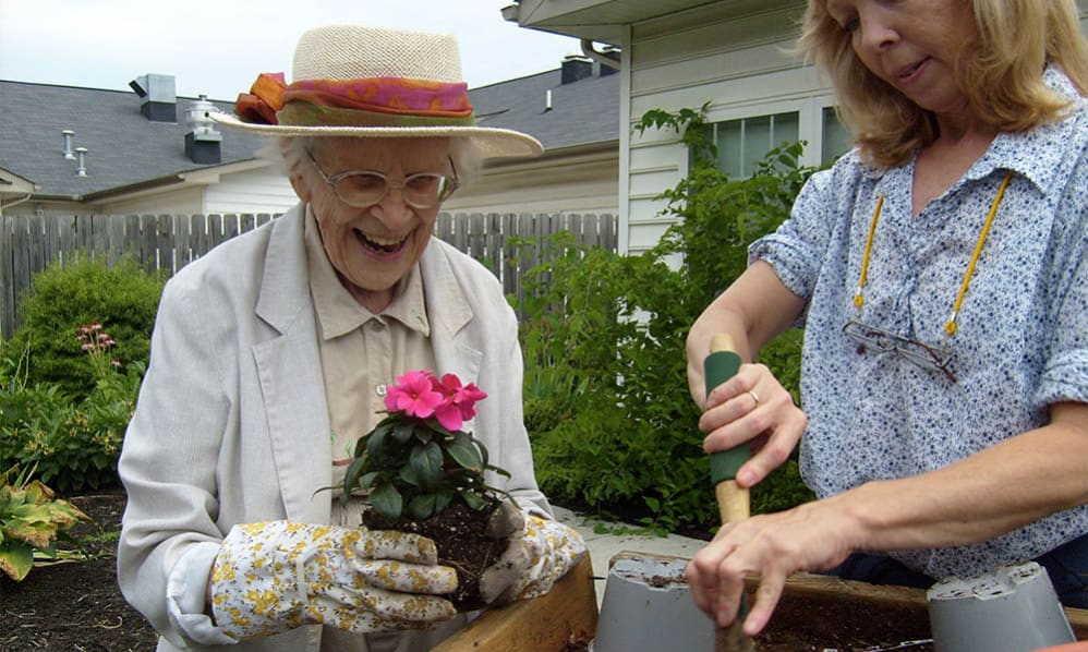 Senior resident planting flowers with staff member outdoors