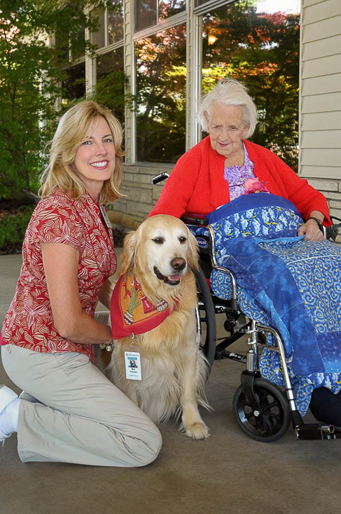 A staff member with a resident and a therapy dog