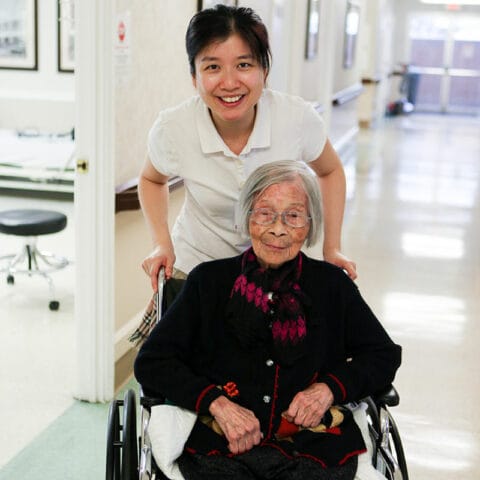 A caregiver smiling behind an elderly resident in a hallway