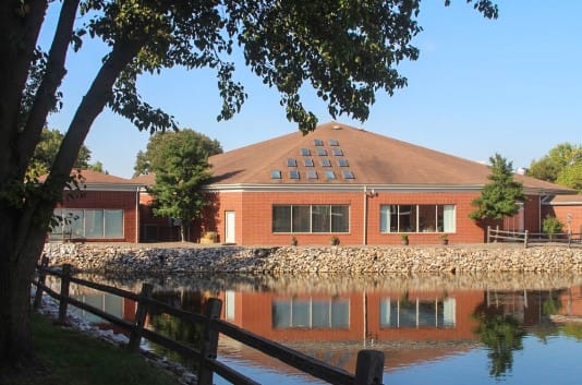 Heritage Center building reflecting in the lake with trees nearby
