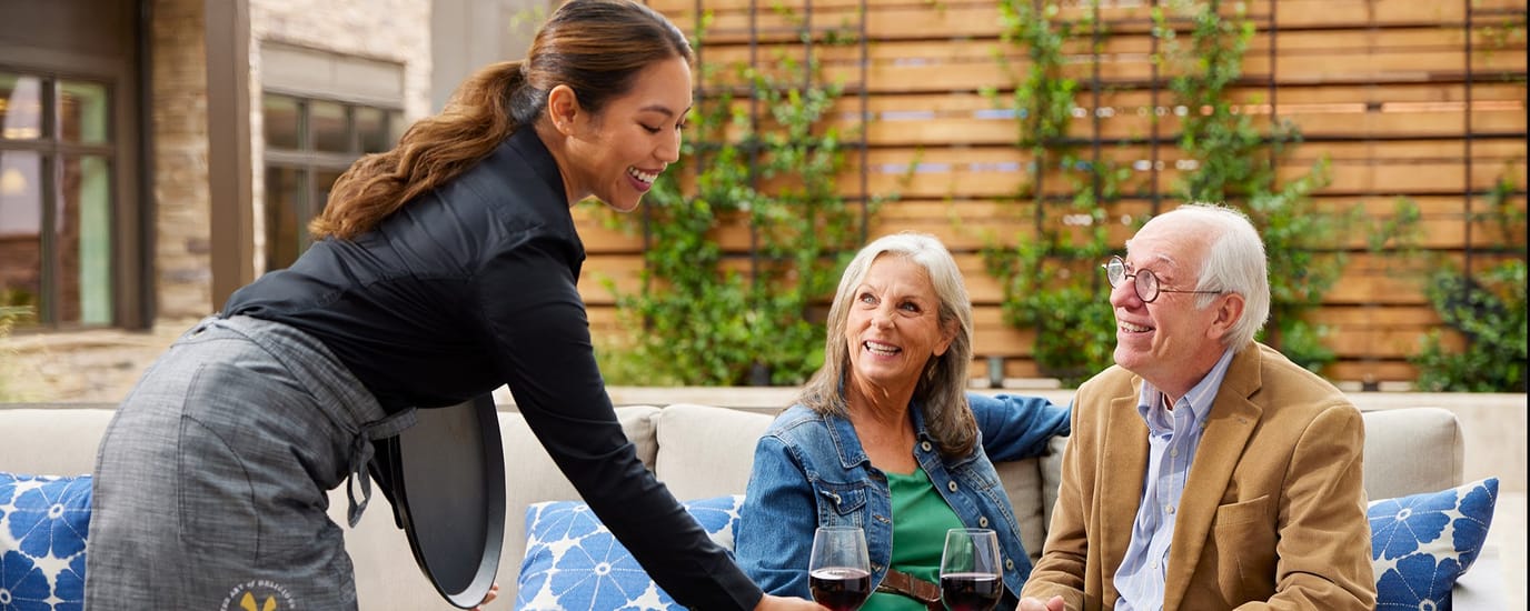 Staff serving wine to smiling residents in an outdoor space