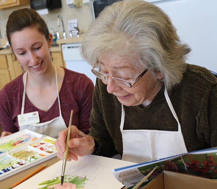 Resident painting with staff assistance in an indoor activity