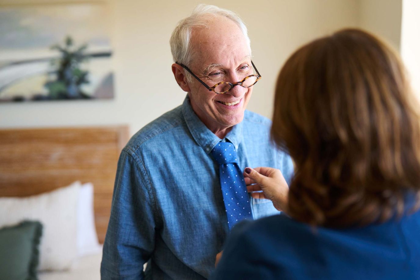 A resident smiling while adjusting his tie with assistance