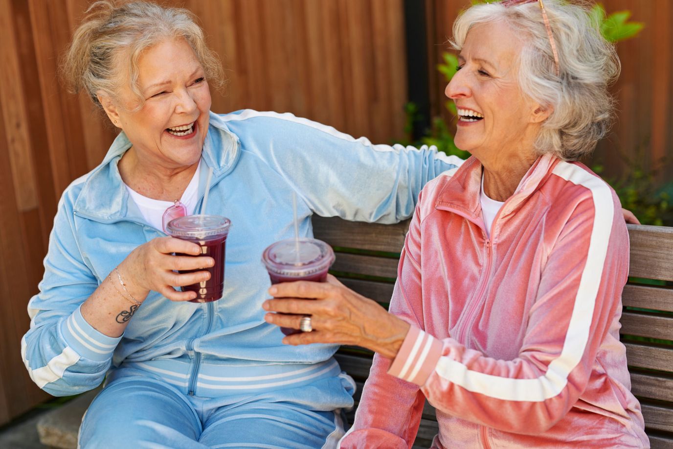 Two smiling women enjoying drinks on a bench