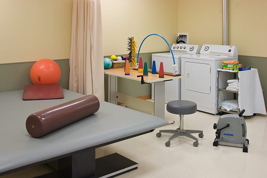 A physical therapy room with exercise equipment and laundry in the background.