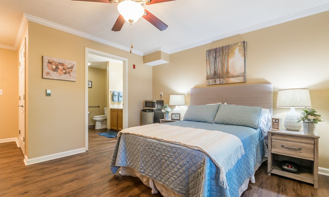 A cozy bedroom featuring a bed with a blue quilt, lamps, and artwork.