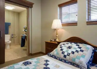 A comfortable bedroom with a quilted bedspread and a view of an attached bathroom.