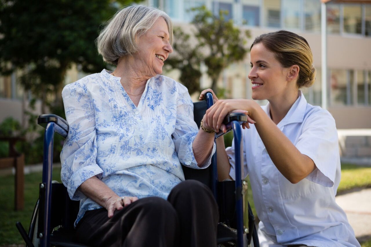 A caregiver smiles with a resident in a wheelchair outdoors