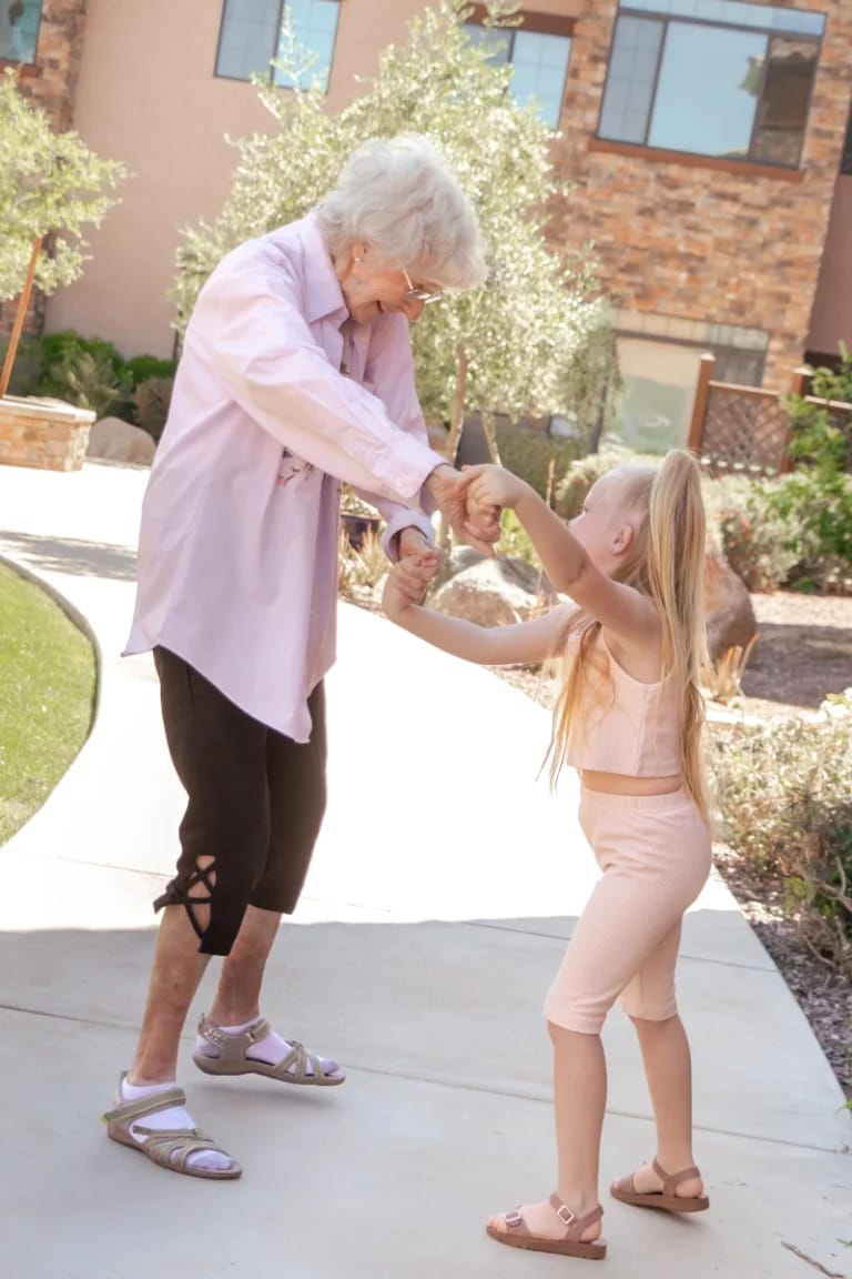 An elderly woman dancing with a young girl outdoors
