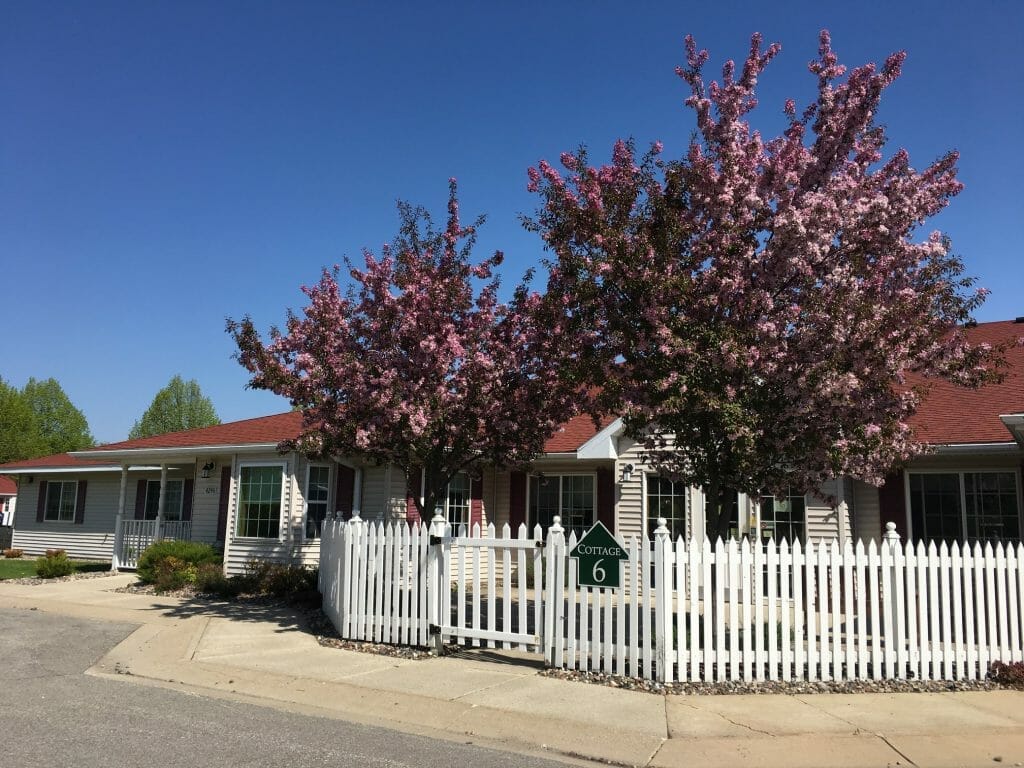 Exterior view of Cottagewood Senior Community with blooming trees and a white fence.