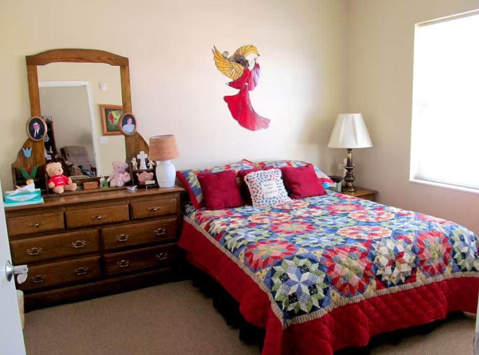 Comfortable bedroom featuring a quilted bed and dresser.