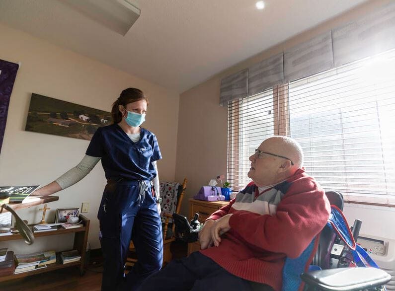 A caregiver talks with a senior resident in a well-lit room.