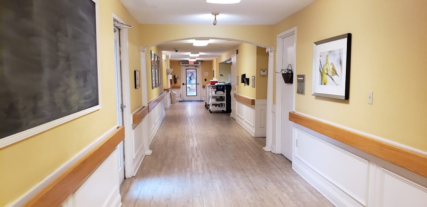 A bright hallway with yellow walls and artwork at Hermitage Care & Rehabilitation Center.