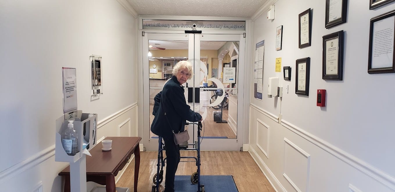 A senior woman using a walker at the facility entrance