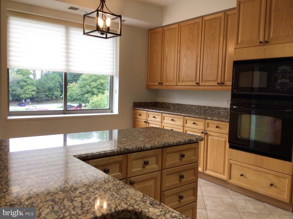 A well-lit kitchen featuring wooden cabinets, granite countertops, and window view.