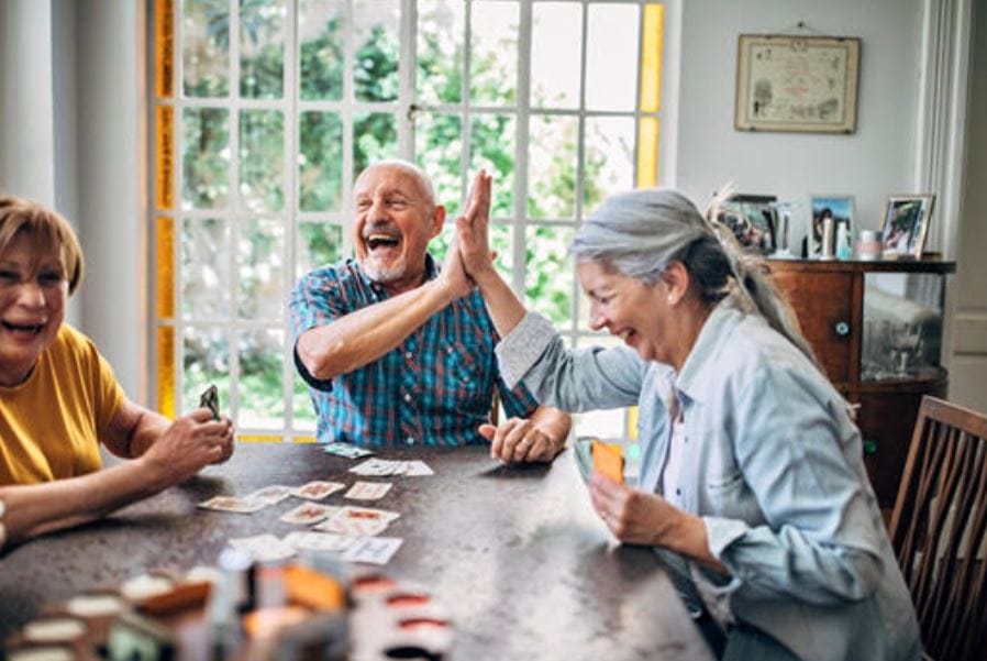Three seniors laughing and playing cards together