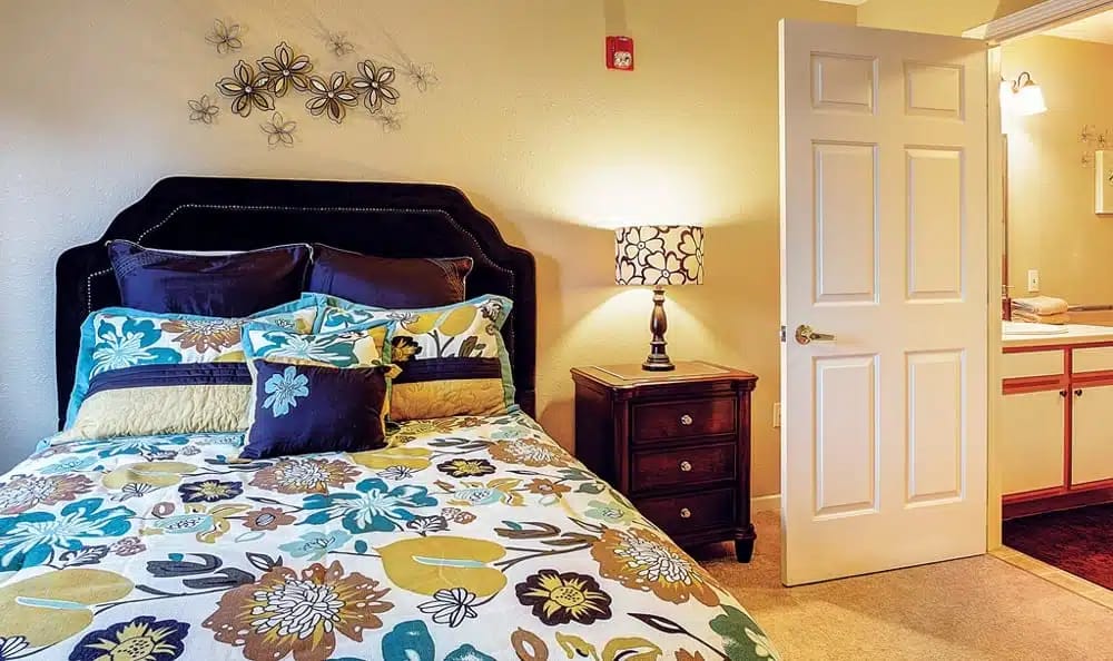 A beautifully decorated bedroom with floral bedding, nightstand, and lamp.
