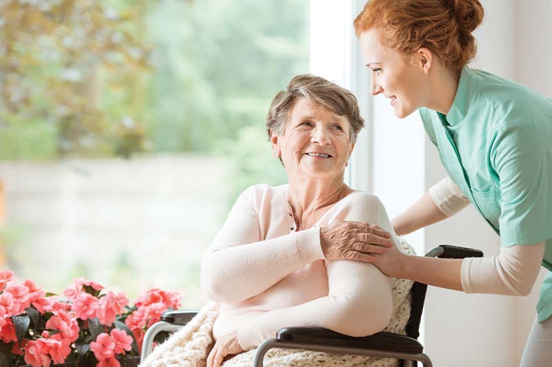 Caregiver assisting a smiling resident in a cozy environment.