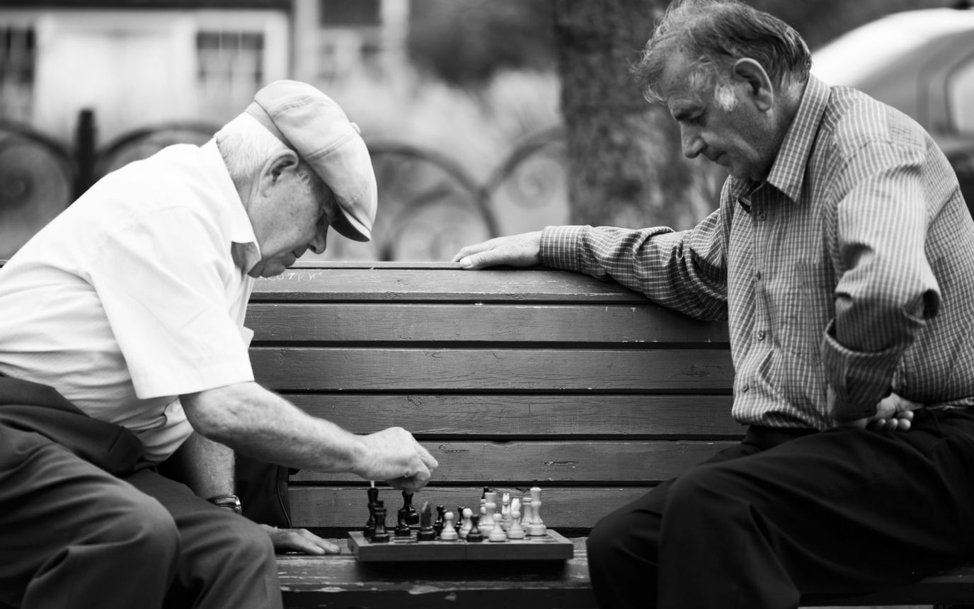 Two elderly men playing chess outdoors.