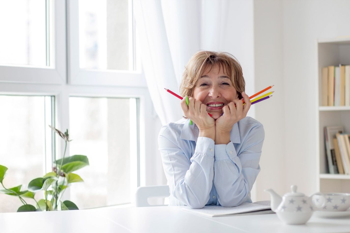 Smiling woman holding colored pencils in a bright room.