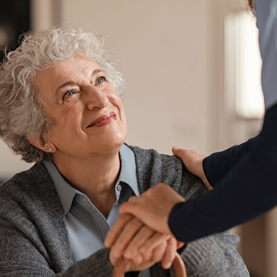 Senior woman smiling, holding hands with a caregiver.