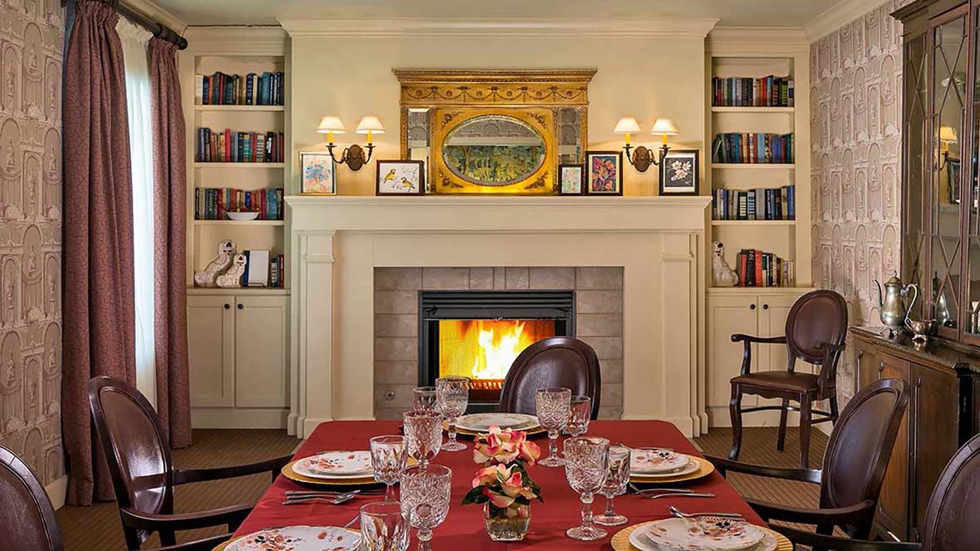Dining room with a red tablecloth, elegant table setting, and a fireplace.