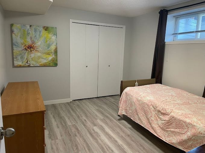 A cozy bedroom featuring a bed, dresser, and artwork.