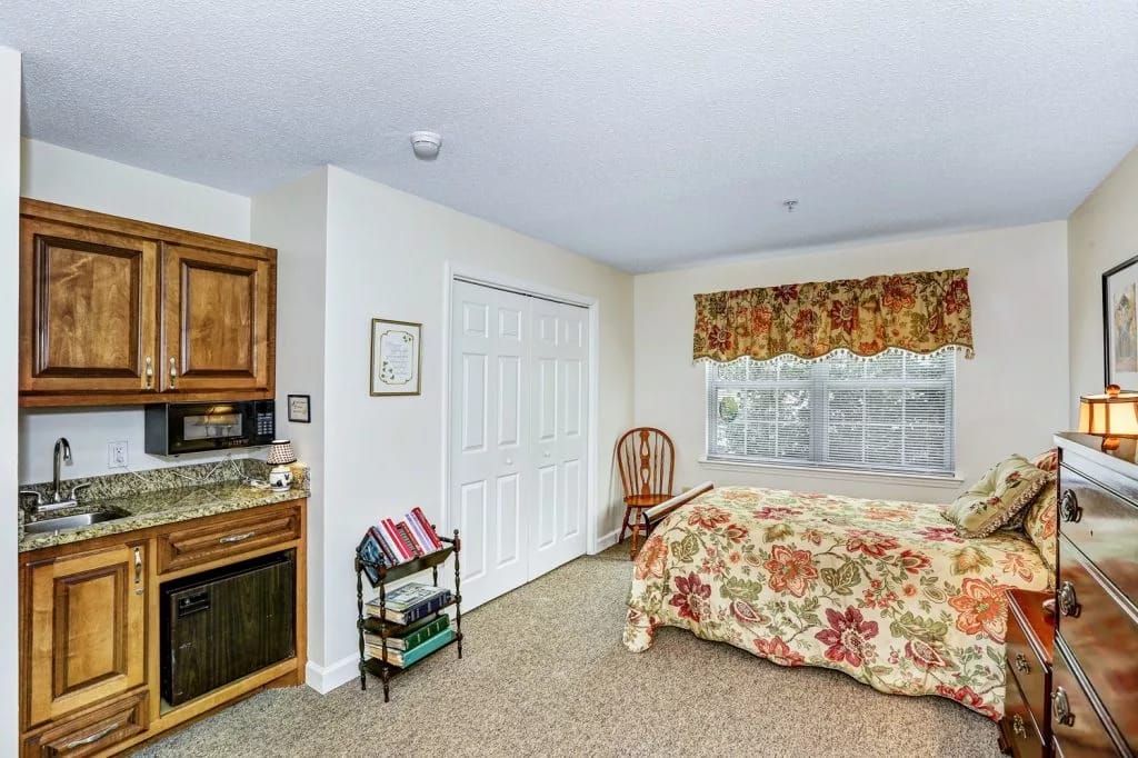 Bright bedroom with floral bedding and kitchenette.