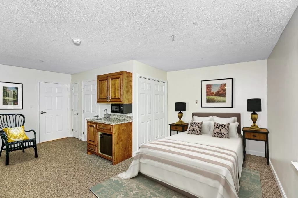 A cozy bedroom with a bed, kitchenette, and seating area.