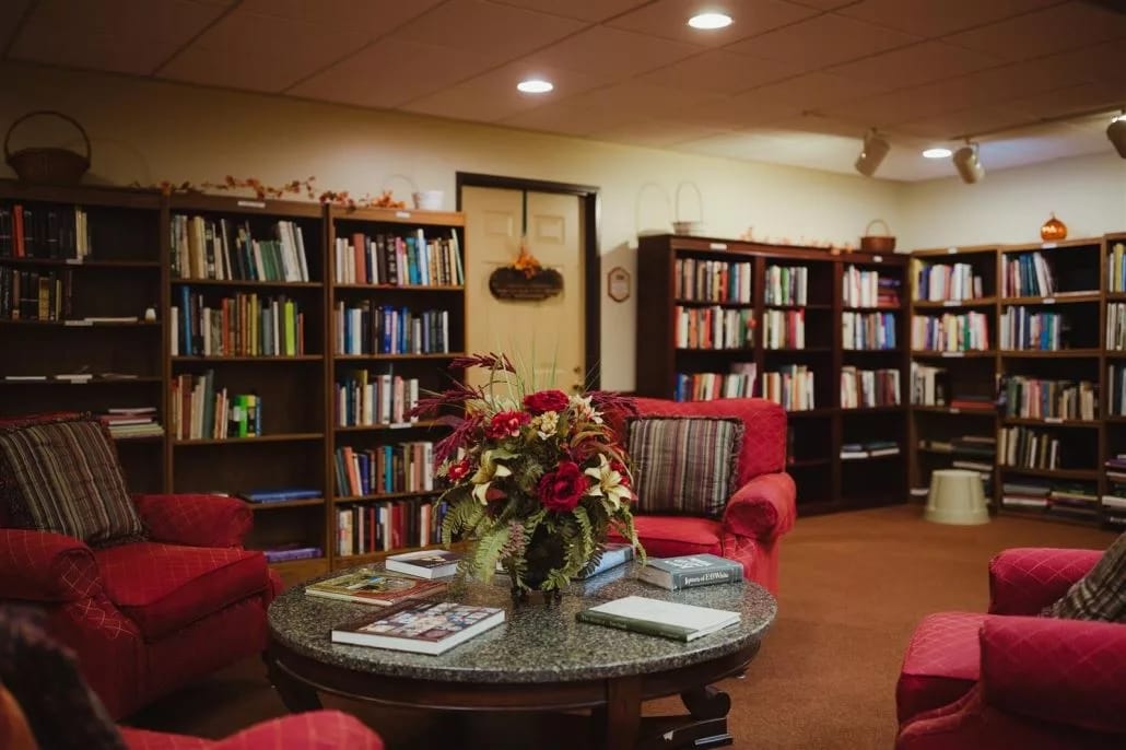 A comfortable library lounge featuring red chairs and bookshelves filled with books.