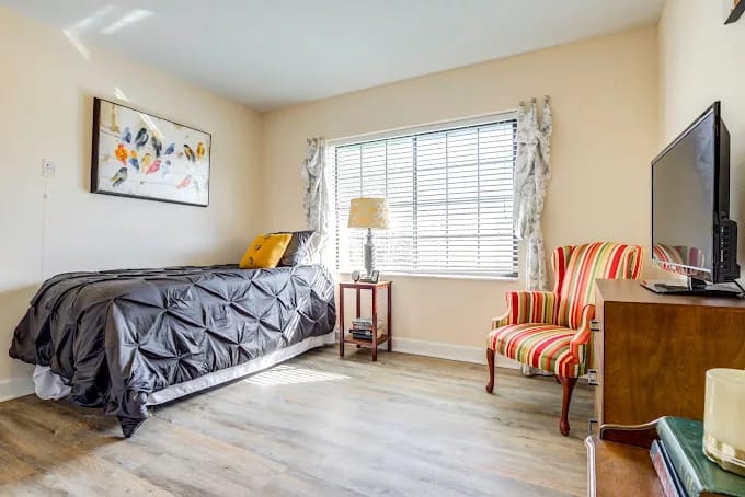 A cozy bedroom featuring a single bed, colorful armchair, and a window with natural light.