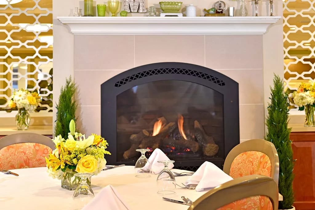 A dining table set with a floral centerpiece by a fireplace
