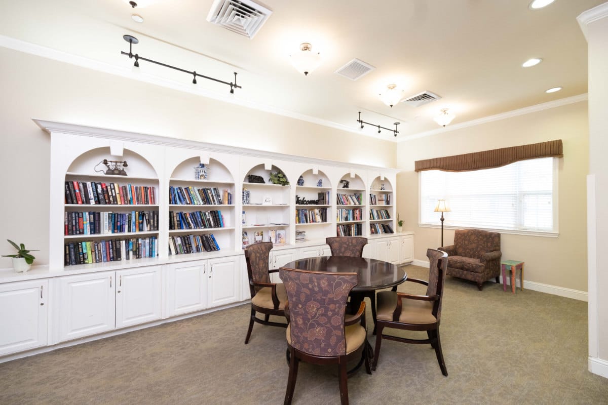 A well-lit library with bookshelves, a round table, and comfortable seating.