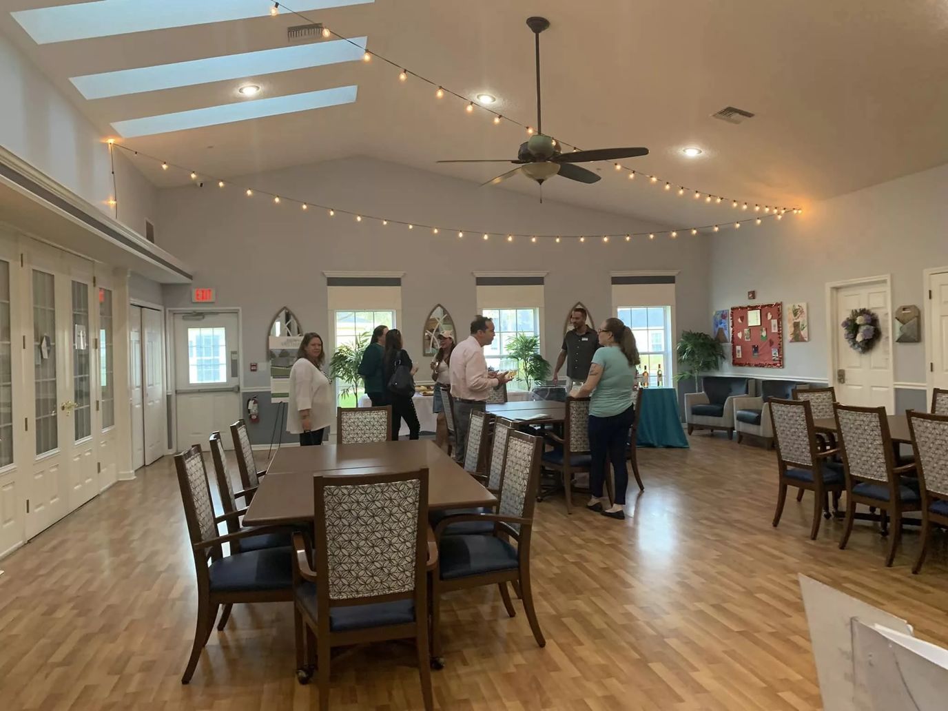 Residents and staff interacting in a well-lit common area with tables and chairs.