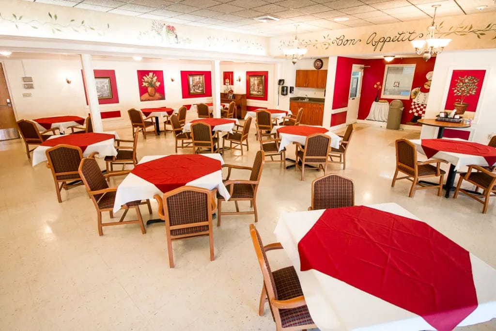 Dining area with red tablecloths and chairs in a senior living facility.