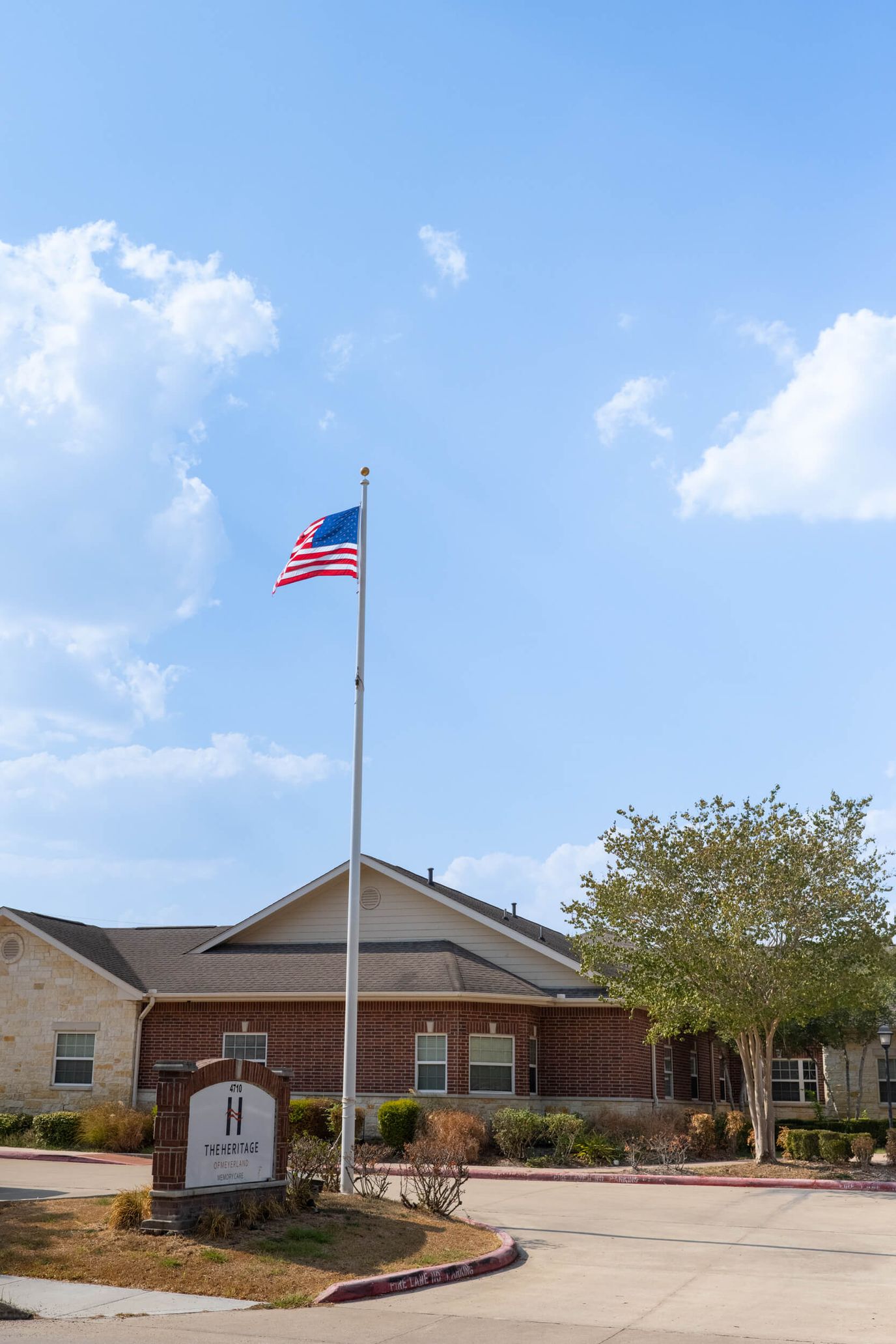 Entrance view of The Heritage of Meyerland with American flag