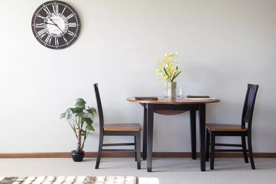 Table setting with two chairs, a plant, and a wall clock