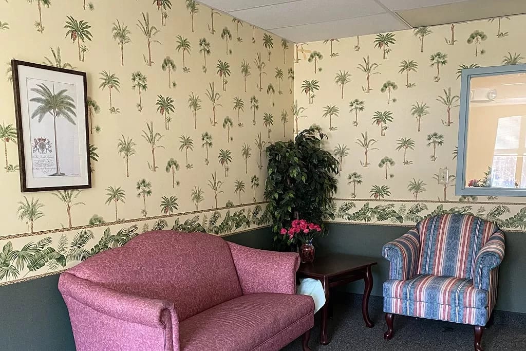A cozy living room with palm-patterned wallpaper, a pink sofa, and a striped armchair.