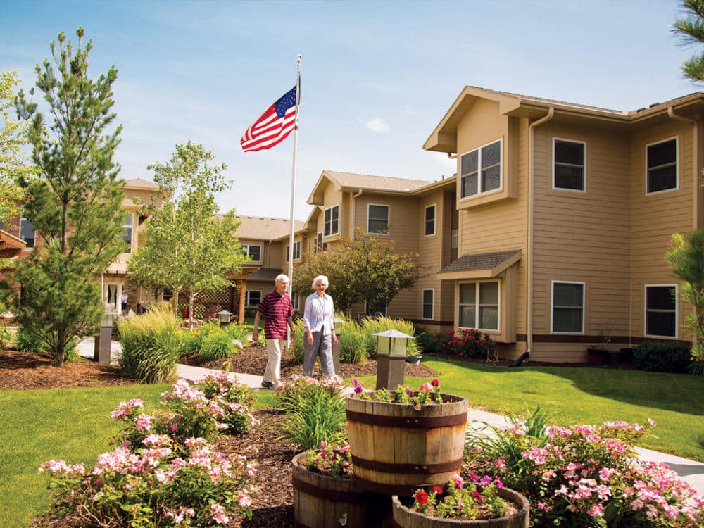 Two seniors walking through a flower garden near their residence
