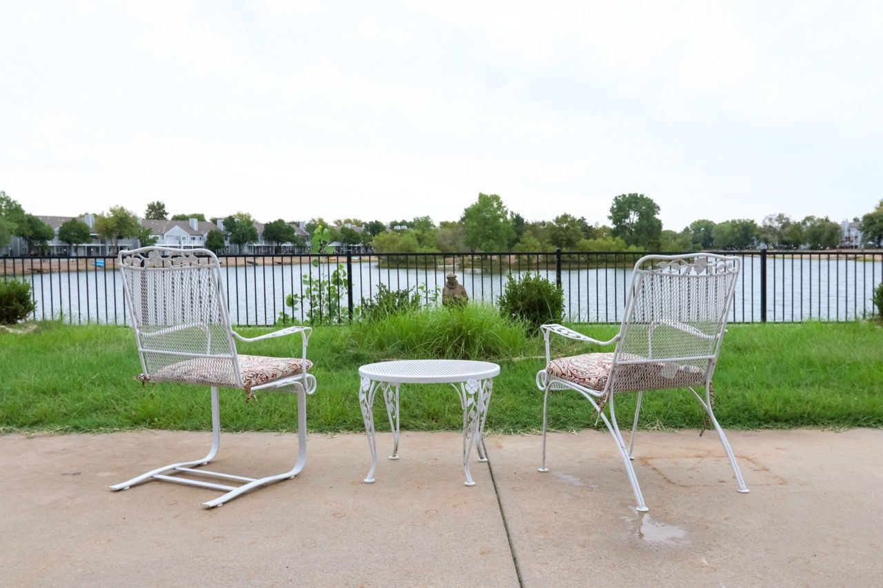 Two white metal chairs and a small table overlooking a lake