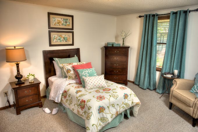 A warmly decorated bedroom with a bed, lamp, and dresser.