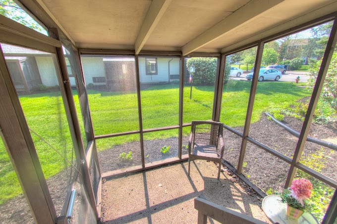 A sunroom with a view of the green lawn and garden.
