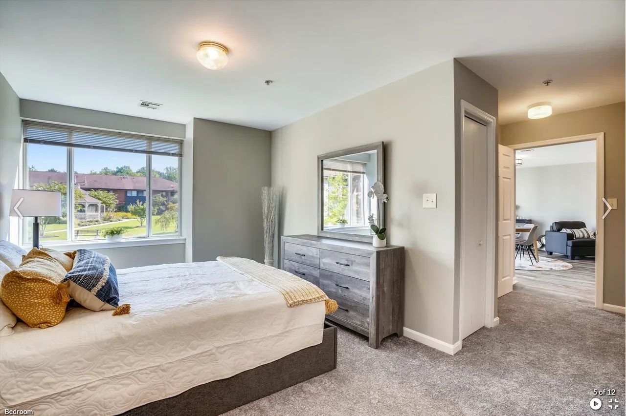 A well-furnished bedroom with a bed, dresser, and large window.